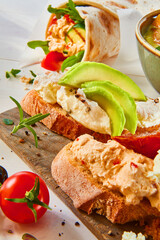 Weizenbrot auf dunklem Holzbrett mit Avocaodo, Frischkäse, Dip, gesund, belegtes Brot, Avocadoscheiben, 