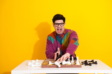 Frustrated Man Overturns Chess Pieces in Displeasure, Expressing Defeat Against Vivid Yellow...