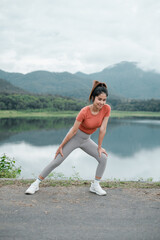 Woman in activewear stretching by a lake with mountains in the background, showcasing fitness and nature.