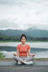 Fototapeta premium A woman practices meditation by a tranquil lake with mountains in the background, creating a peaceful and serene atmosphere.