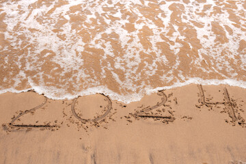 Year 2024 written on sand washed away by sea wave