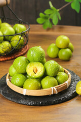 Fresh Green Sichuan Plums in Bamboo Basket with Water Droplets on Rustic Wooden Table