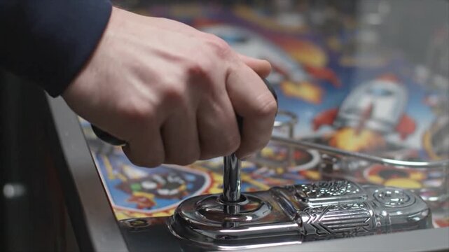 Captures a persons hand pulling back the plunger on a pinball machine, suitable for illustrating arcade games or retro entertainment themes.