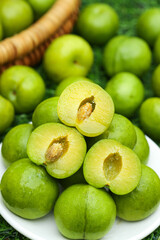 Fresh Green Plums Cut in Half Showing Yellow Flesh and Pit in White Bowl