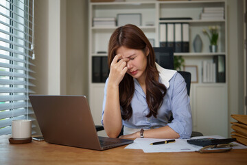 Tired female employee suffering from headache or burnout while working on computer in modern workplace.