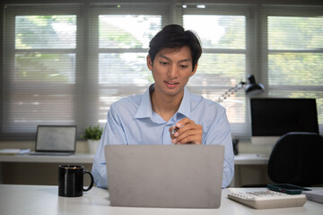 Businessman using laptop and calculator while analyzing business data at workplace.