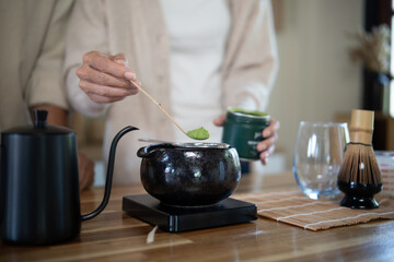 Hands of a couple making Japanese matcha together, adding green tea powder with a bamboo scoop in a cozy kitchen.