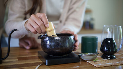 Close up of woman whisking matcha in a ceramic bowl during a traditional tea preparation.