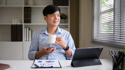 Young businessman enjoying coffee break in office with digital devices and documents.