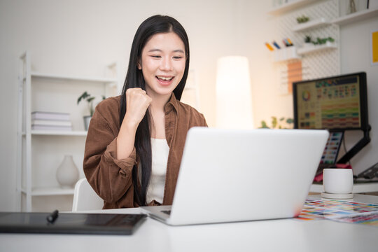 Excited young graphic designer celebrating success while working on a laptop in a creative modern office.