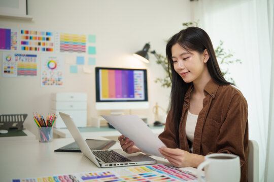 Smiling young graphic designer working with color swatches at a modern desk.