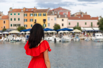 Woman in red dress looking at colorful harbor. Back view of a woman in a red dress standing by the water, gazing at boats and colorful waterfront buildings.