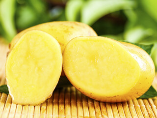 Fresh Yellow Potatoes Cut in Half on Bamboo Mat with Green Vegetables