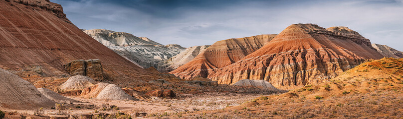 Panoramic view of colorful mountains rising from dry desert landscape under cloudy sky in Kazakhstan © EdNurg