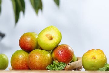 Fresh Ripe Plums Cut in Half Showing Yellow Flesh with Red Green Skin and Mint Leaves