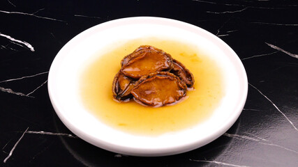 Small Fresh Dried Abalone Seafood Delicacy on White Plate with Golden Sauce