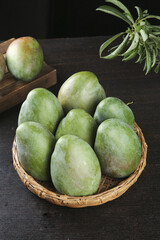 Fresh Green Mangoes from Sichuan Panzhihua in Wicker Basket on Dark Wood Background