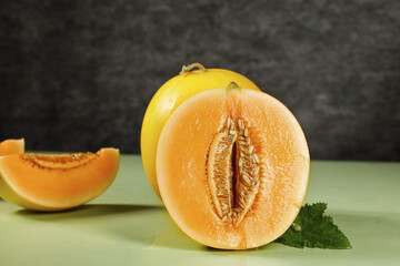 Fresh Cut Honeydew Melon with Sweet Orange Flesh and Seeds on Green Surface