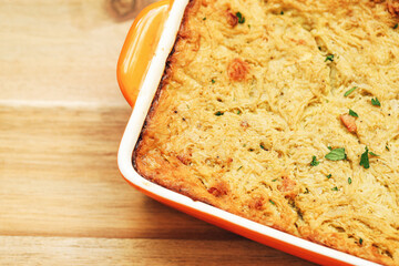Baked casserole in orange dish. Delicious homemade meal on wooden table. Golden crust with herbs. Traditional comfort food freshly prepared. Tasty dinner idea with natural ingredients.