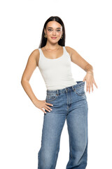 Obraz premium Studio shot of young woman with long dark hair wearing white tank top and loose blue jeans holding waistband to show fit on white background.