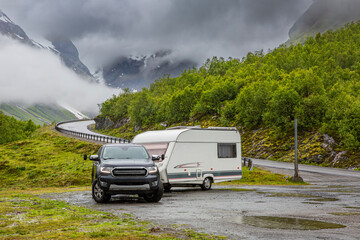 A pickup truck with a camping trailer stands on a mountain road, caravanning