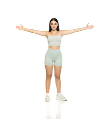 Studio shot of full length young woman in mint green activewear and white sneakers, standing with arms extended horizontally for anatomical or fitness pose on white background. © vladimirfloyd