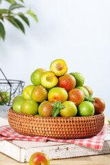 Fresh Red and Green Plums in Wicker Basket on Rustic Kitchen Table with Checkered Cloth