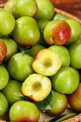 Fresh Green Plums with Red Blush Cut in Half Showing Yellow Flesh in Wicker Basket Display