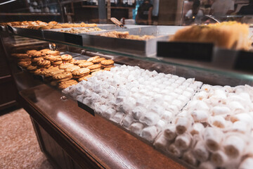 An appetizing view of a wide variety of traditional sweets, including powdered sugar delights and buttery cookies, neatly arranged in a glass display case at a bakery.