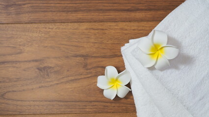 White frangipani flowers placed on folded towels over wooden background, symbolizing tropical spa, relaxation, wellness, and natural beauty, perfect for health and hospitality concepts.