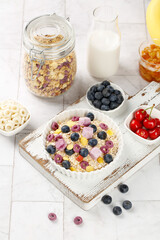 Healthy oatmeal breakfast bowl with berries yogurt chunks and milk on white wooden background top view