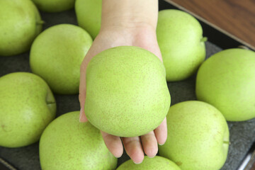 Fresh Green Apple in Hand with Jade Colored Fruit Display on Wooden Surface