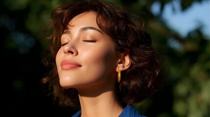 A beautiful, content woman with her eyes closed, basking in the warm, natural light of the outdoors and surrounded by the peaceful natural environment