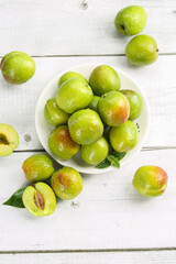 Fresh Green Plums with Red Blush in White Bowl on Wooden Background - Healthy Organic Fruit