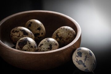 Small quail eggs in a wooden bowl on a dark table