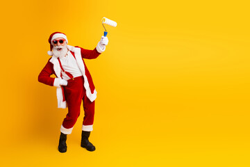 Santa Claus enjoying holiday fun with a creative paint roller gesture against a vibrant yellow backdrop in festive spirit