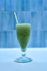 Green smoothie stands on white table with blue tile backdrop
