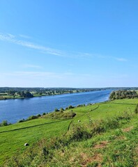 Obraz premium River landscape with green meadow and blue sky