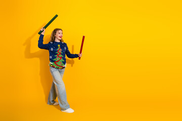 Cheerful young woman wearing a festive Christmas sweater, enthusiastically posing on a bright yellow background