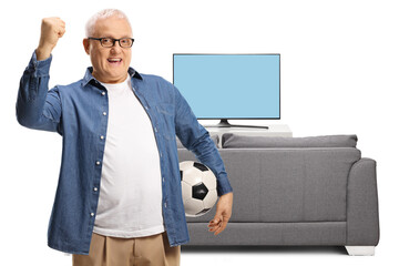 Football team supporter holding a ball and gesturing with hand in front of tv