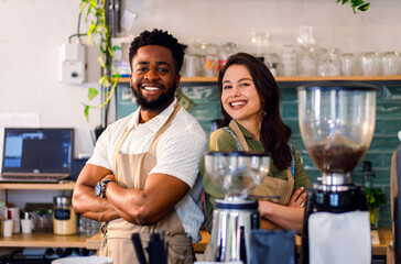Portrait of male and female barista standing in her coffee shop behind the counter looking at camera.