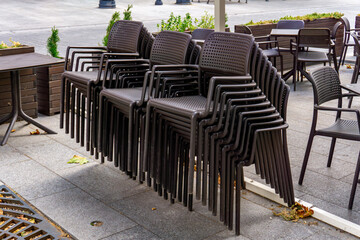 Stacks of brown plastic chairs arranged outside café, with tables and plants visible in background.