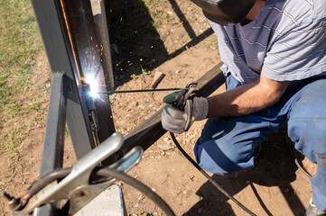 Male welder working outdoors with protective gear and welding equipment on metal structure. National Welding Month