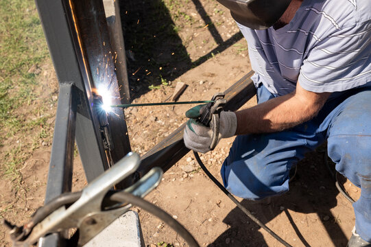 Male welder working outdoors with protective gear and welding equipment on metal structure. National Welding Month - Powered by Adobe