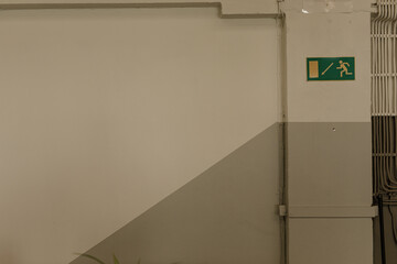 Stock photo of a beige wall with an emergency exit sign, pipes, and a diagonal color separation.