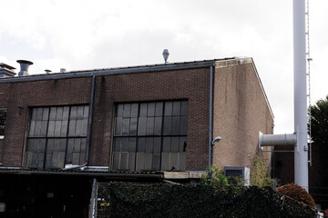 Stock photo of an aged brick industrial building, featuring large windows and a tall pipe. Perfect for concepts of industry, history,