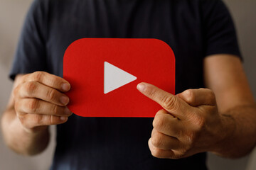 Close-up of a person's hands holding a red YouTube play button.  Perfect for social media, video marketing, and online content.