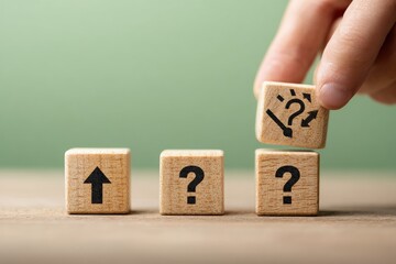 A hand places a wooden block with a question mark and arrows on top of three other blocks, two displaying question marks and one an upward arrow