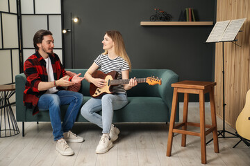 Tutor teaching woman to play guitar on sofa at home