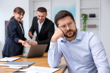 Man feeling jealous of his colleague's success in office, selective focus